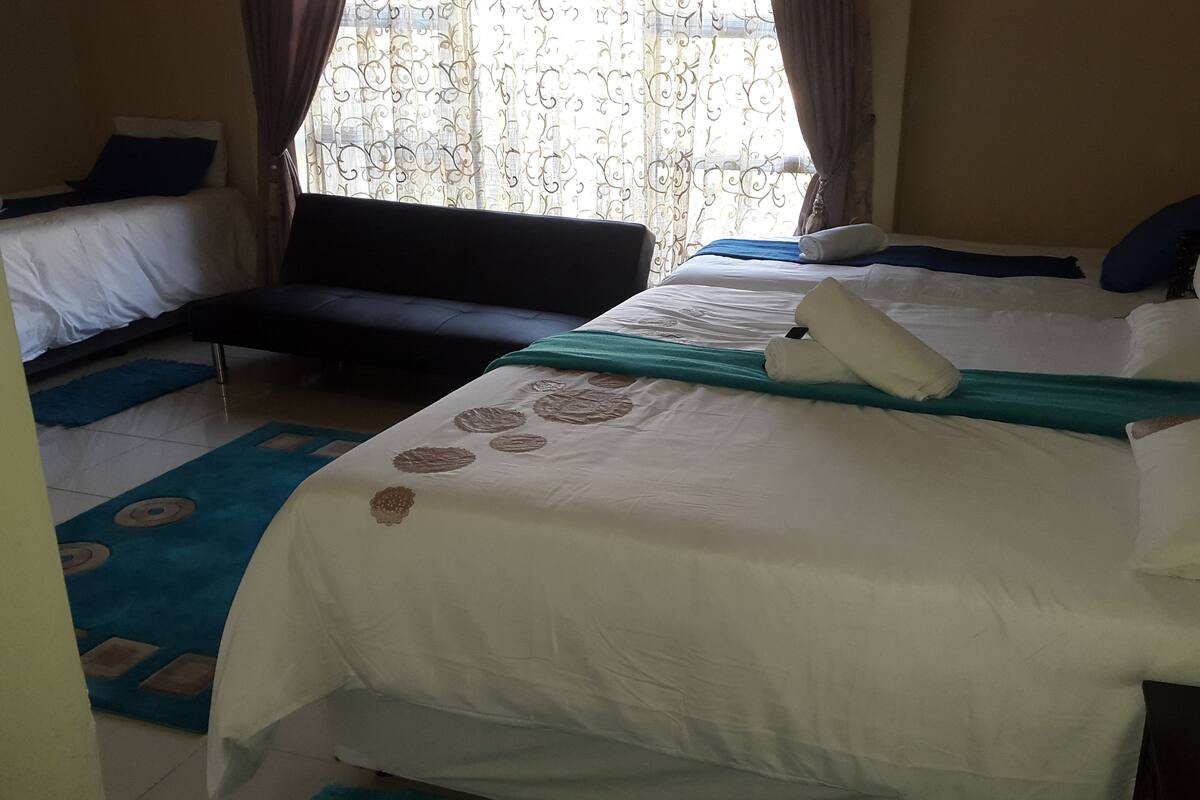 Una habitación de hotel con una cama grande, un sofá y un ventanal con cortinas.
