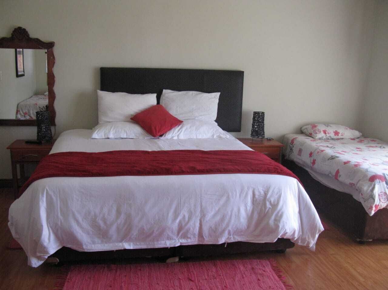 Un dormitorio con una cama grande, una cama más pequeña, una mesita de noche, un aparador y un espejo.