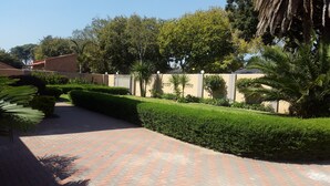 A paved pathway leading through a well-maintained garden with neatly trimmed hedges and a variety of trees.