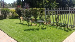 A well-maintained outdoor seating area with a metal fence, a paved walkway, and lush greenery.