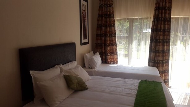 A hotel room with two beds, a framed picture on the wall, and a window with patterned curtains.