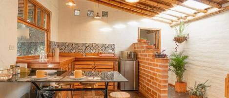 A kitchen with a wooden ceiling, a tiled backsplash, and a brick accent wall. There are stools, a table, and a refrigerator.