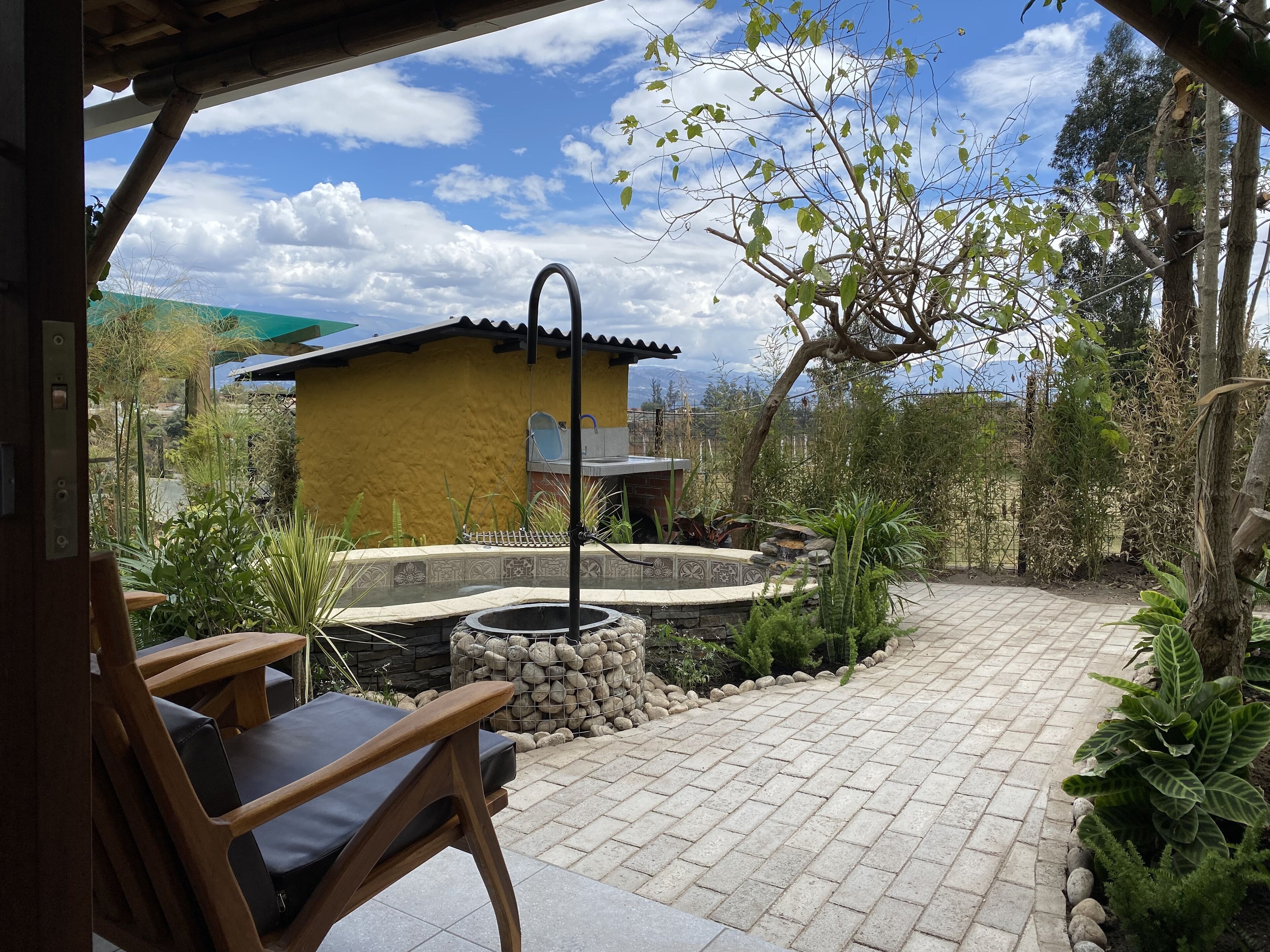 Un patio con suelo de losas de piedra, una piscina pequeña y una silla de madera.
