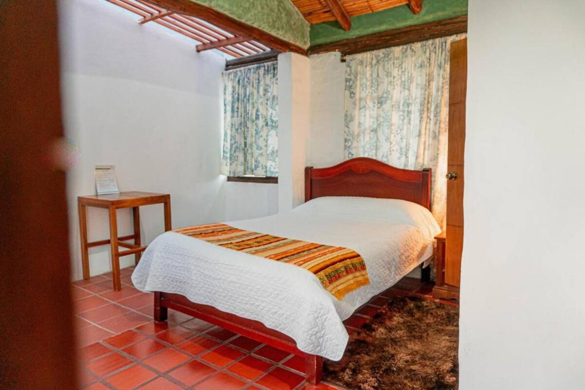 A bedroom with a wooden bed, a small table, and a window with curtains.