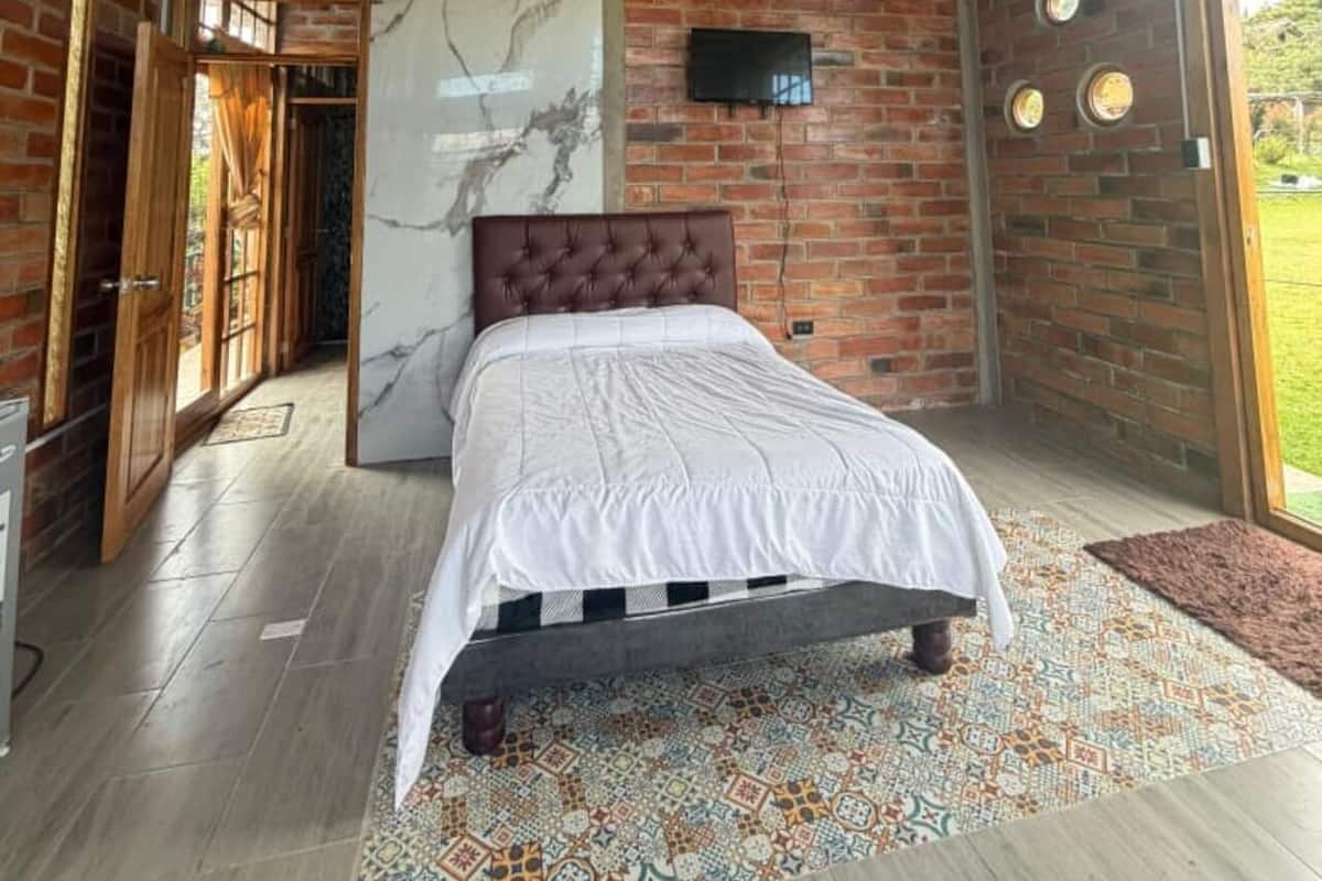 A bedroom with a bed, a TV, a marble wall, and a brick wall.