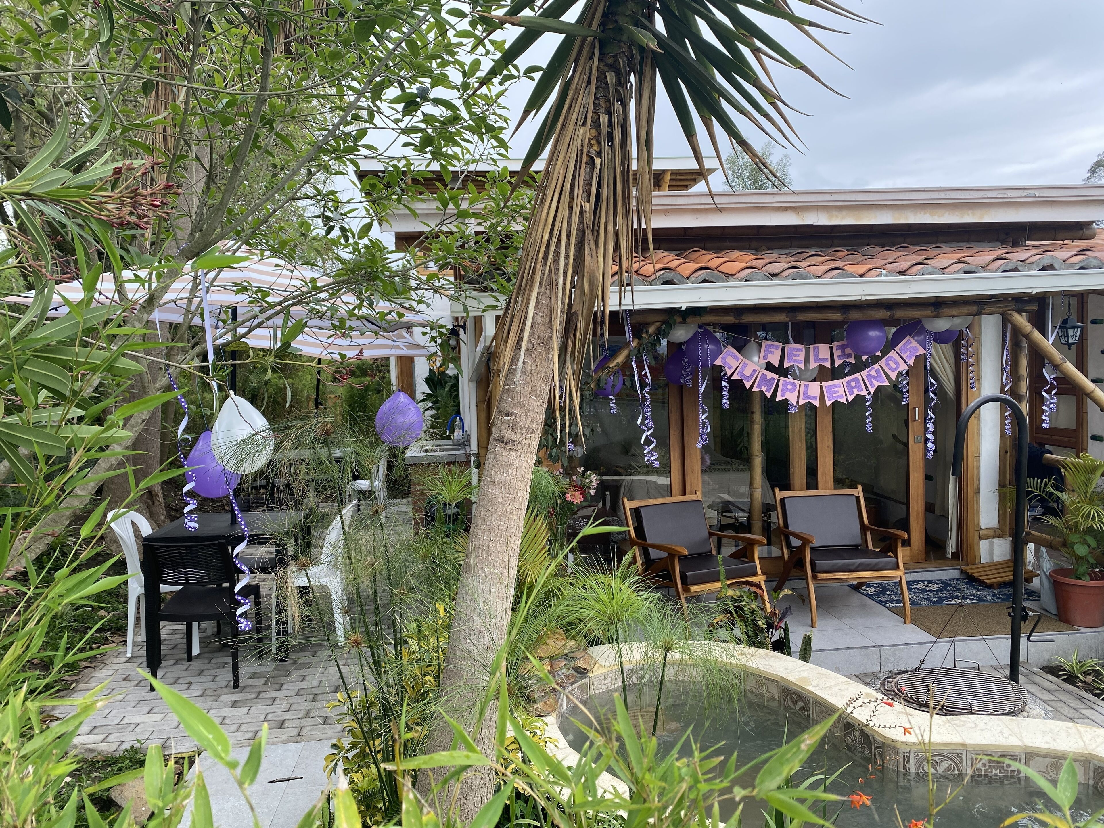 A patio area with outdoor seating, a decorative fountain, and a pergola with a 'FELICIDADES' banner.