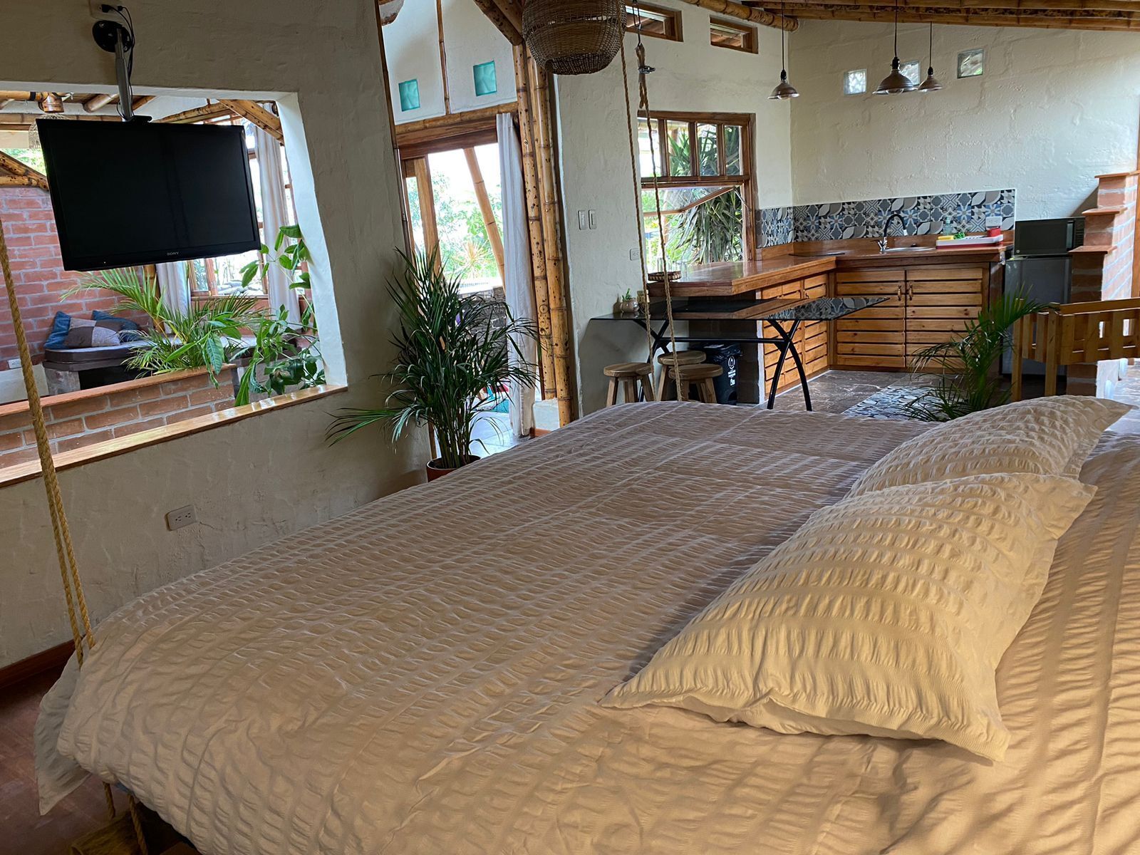 A bedroom with a large bed, a TV, a kitchen area, and a view of the outdoors.