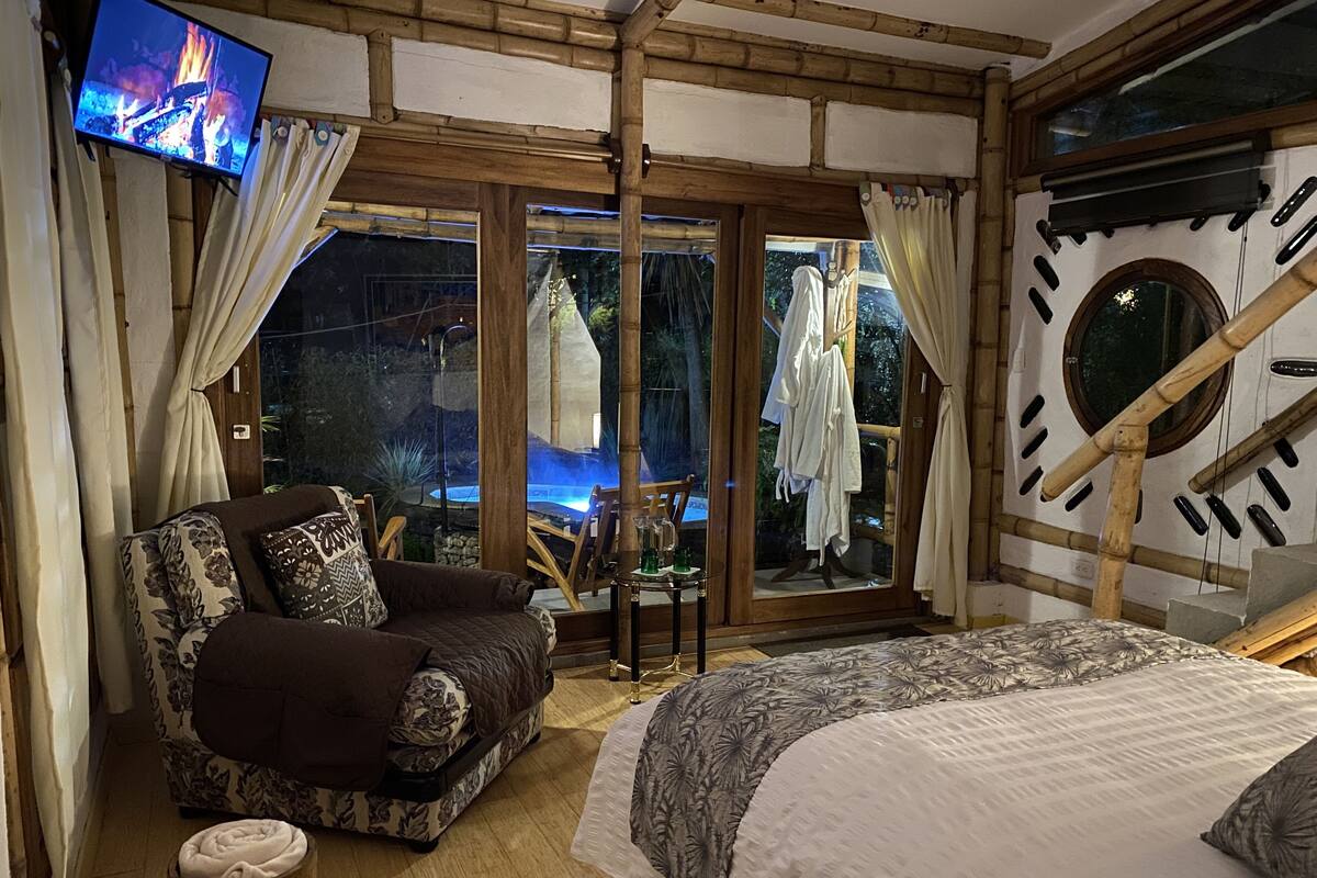 A cozy room with a sofa, a bed, a TV, and a view of a pool and trees.
