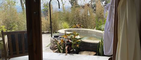A view from inside a room to an outdoor garden area with a hot tub, surrounded by plants and a wooden deck.