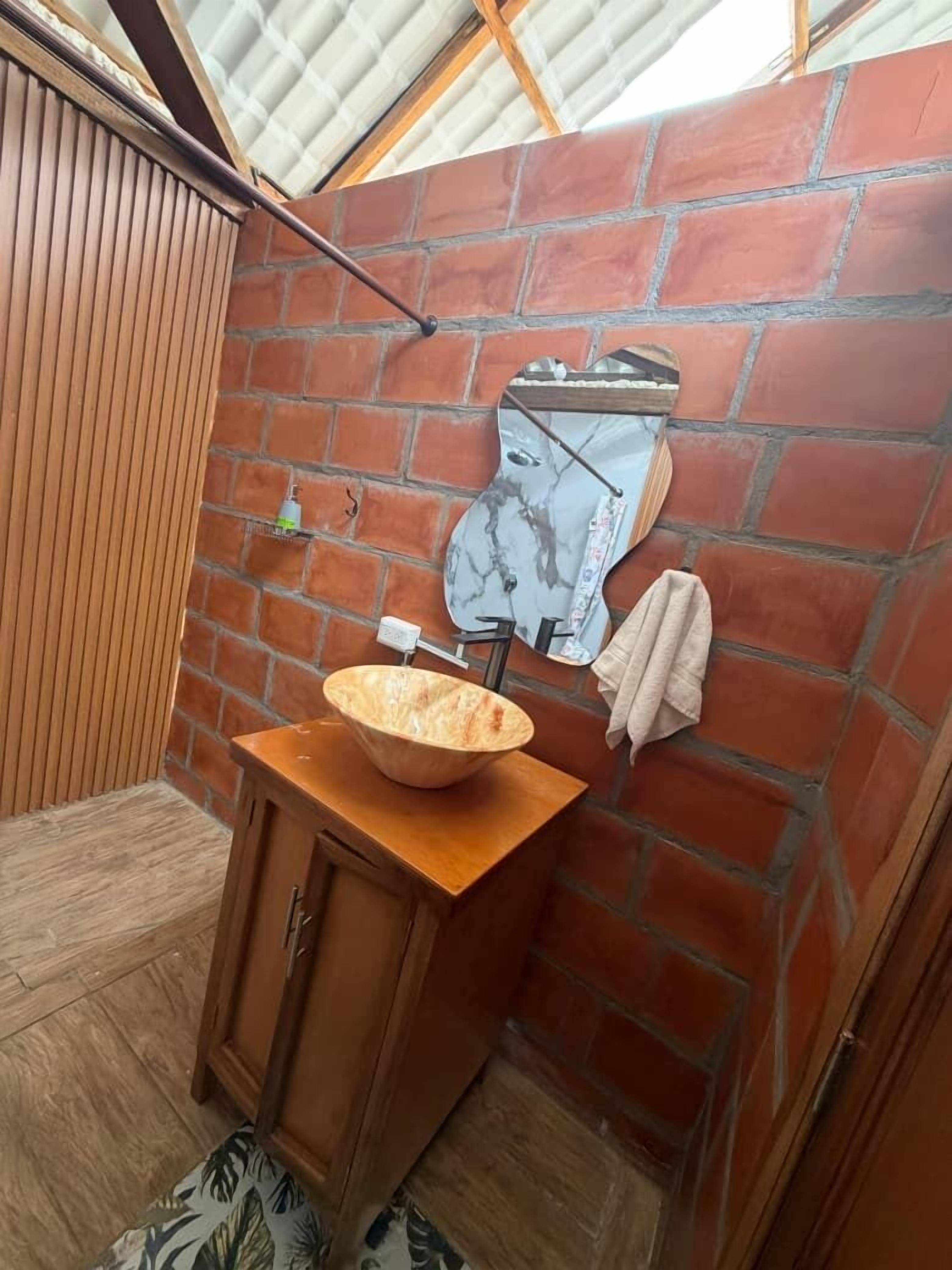 A bathroom with a wooden vanity, a large bowl sink, a towel hanging on the wall, and a mirror.