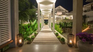A well-lit pathway leading to a building with a modern architectural design, surrounded by lush greenery and outdoor seating areas. - Sri Sharavi Beach Villas & Spa (Thalaramba)