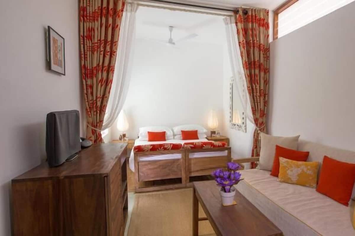 A room with a bed, a sofa, a TV, and a small table with a vase of flowers.