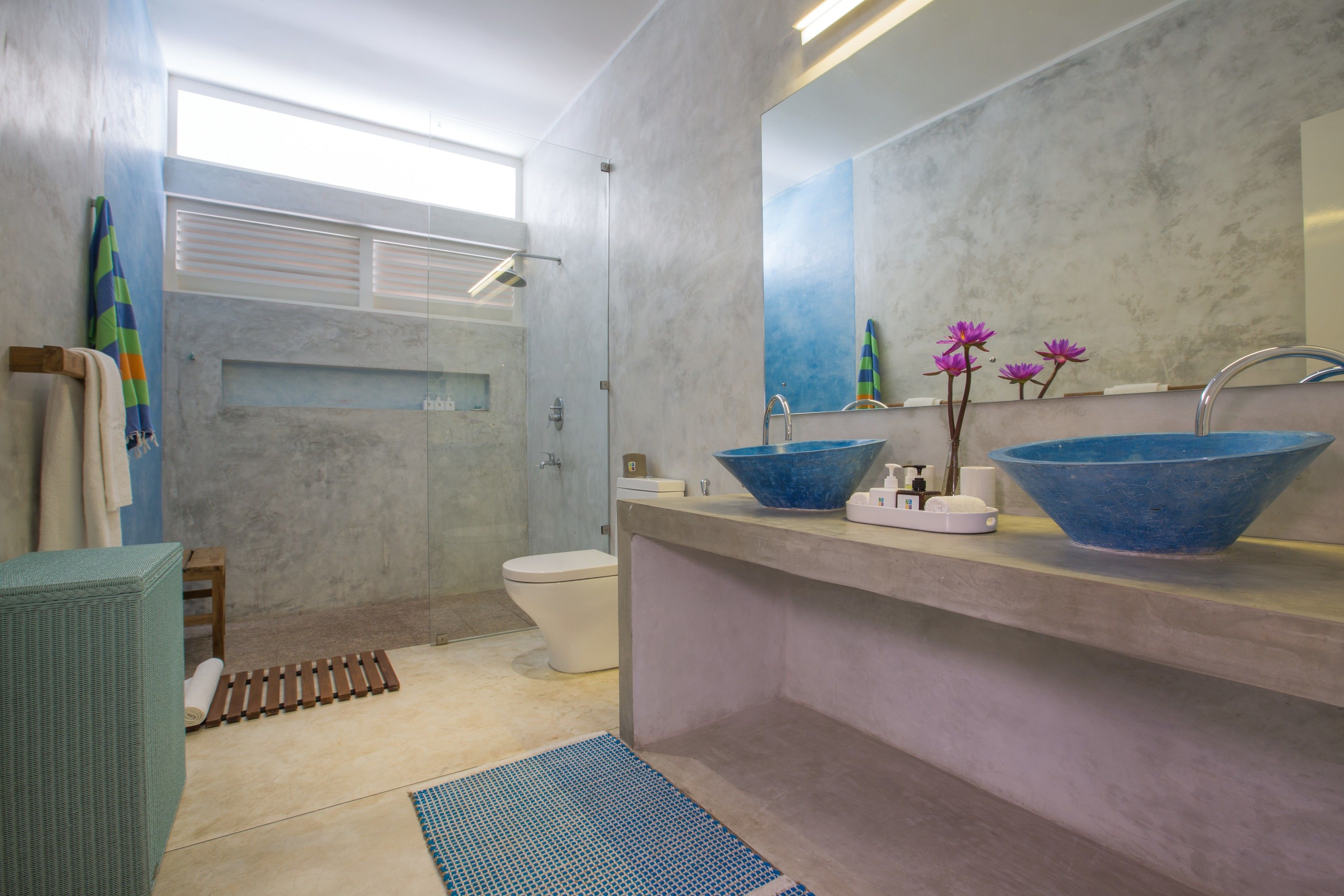 A modern bathroom with a large mirror, two blue sinks, a shower, and a toilet.