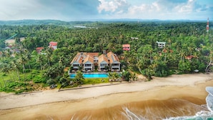 A beachfront property with a pool, surrounded by lush greenery and palm trees, featuring multiple buildings with red roofs. - Sri Sharavi Beach Villas & Spa (Thalaramba)