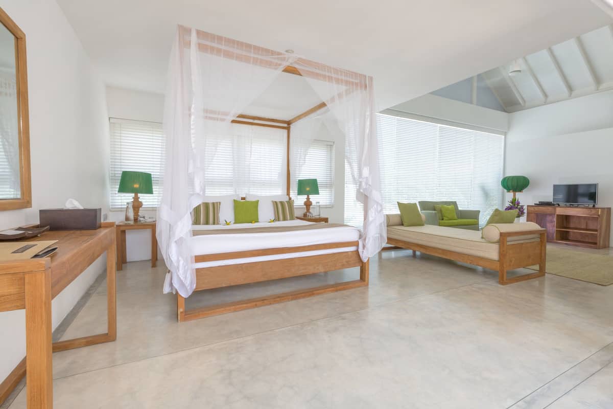 A spacious bedroom with a four-poster bed, a sofa, a desk, and a TV.