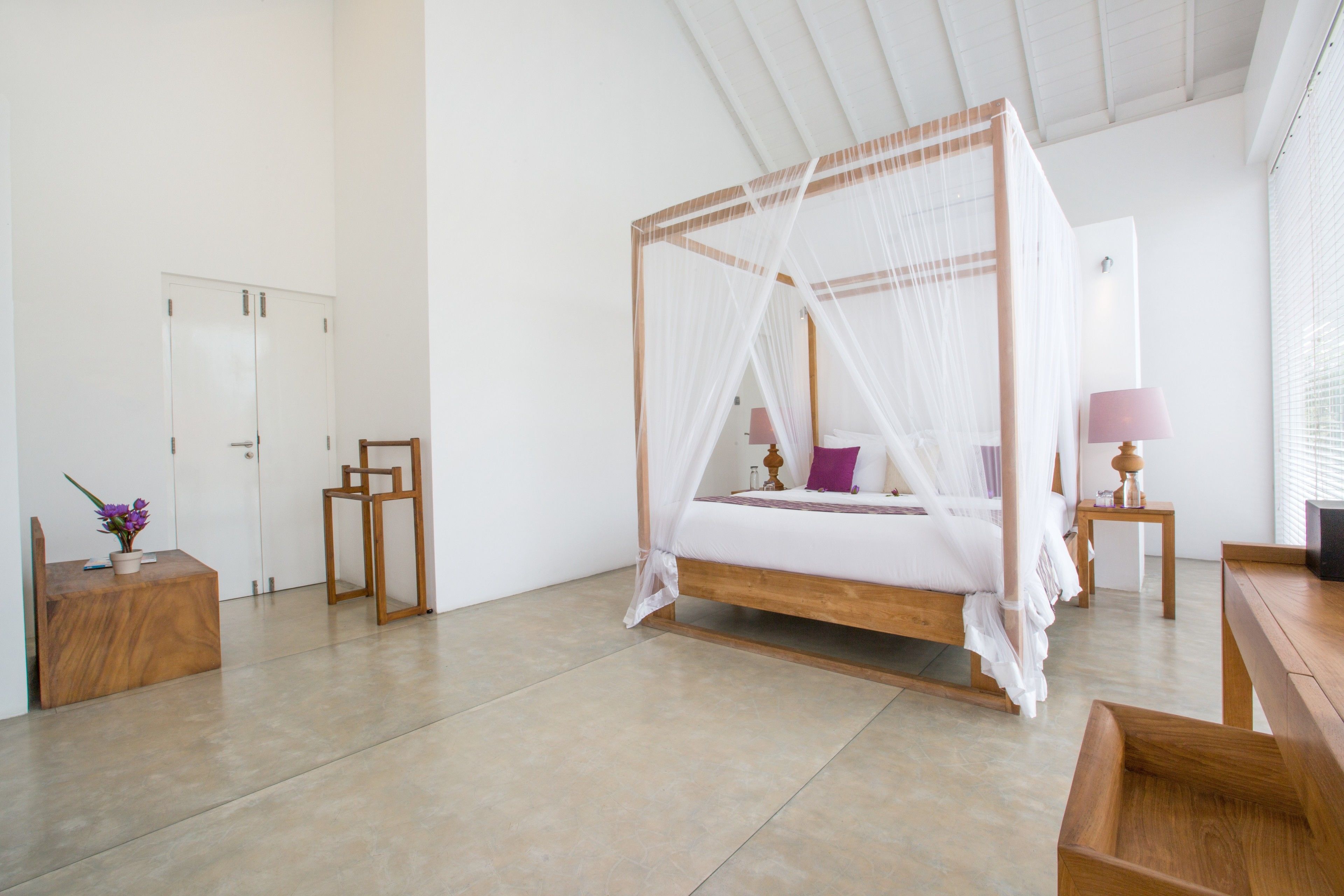 A spacious room with a four-poster bed, a bedside table, a nightstand, and a small wooden bench.