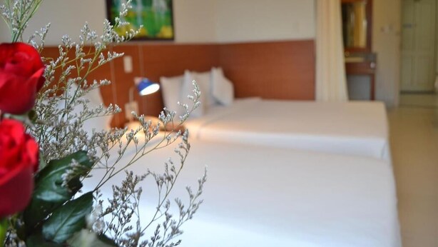 Une chambre d’hôtel avec un lit, une table de chevet et un vase de fleurs.