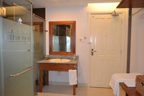 A bathroom with a glass shower enclosure, a sink with a mirror above it, and a white door. - Nemo Hotel (Da Nang)