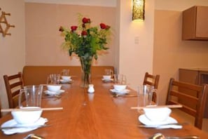 Mesa de comedor preparada para cuatro personas, con vajilla blanca y un florero con flores rojas.