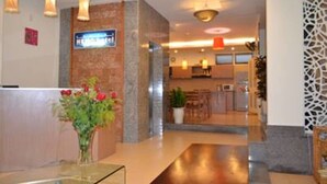 Un espace d’accueil d’hôtel comprenant un comptoir de réception, un vase de fleurs et un panneau au-dessus du comptoir.