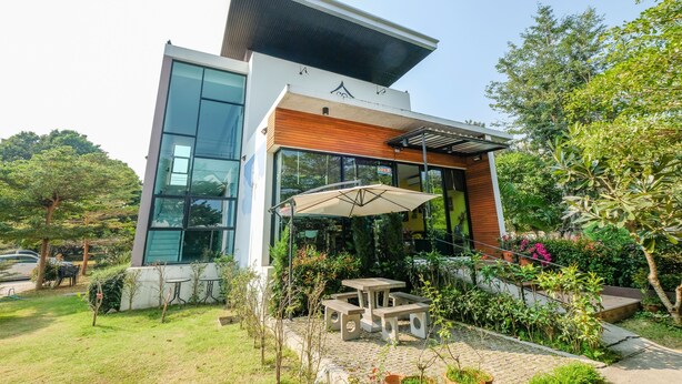 A modern building with a glass facade, a wooden section, and a patio area with outdoor seating.