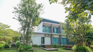 A modern two-story building with a flat roof, surrounded by lush greenery and a well-maintained garden.