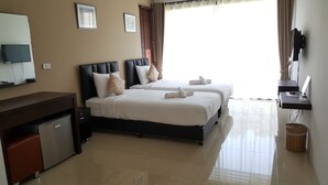A hotel room with two beds, a desk, a TV, and a small kitchenette.