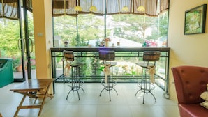 A room with a balcony, two bar stools, a wooden table, a red sofa, and a view of greenery outside.