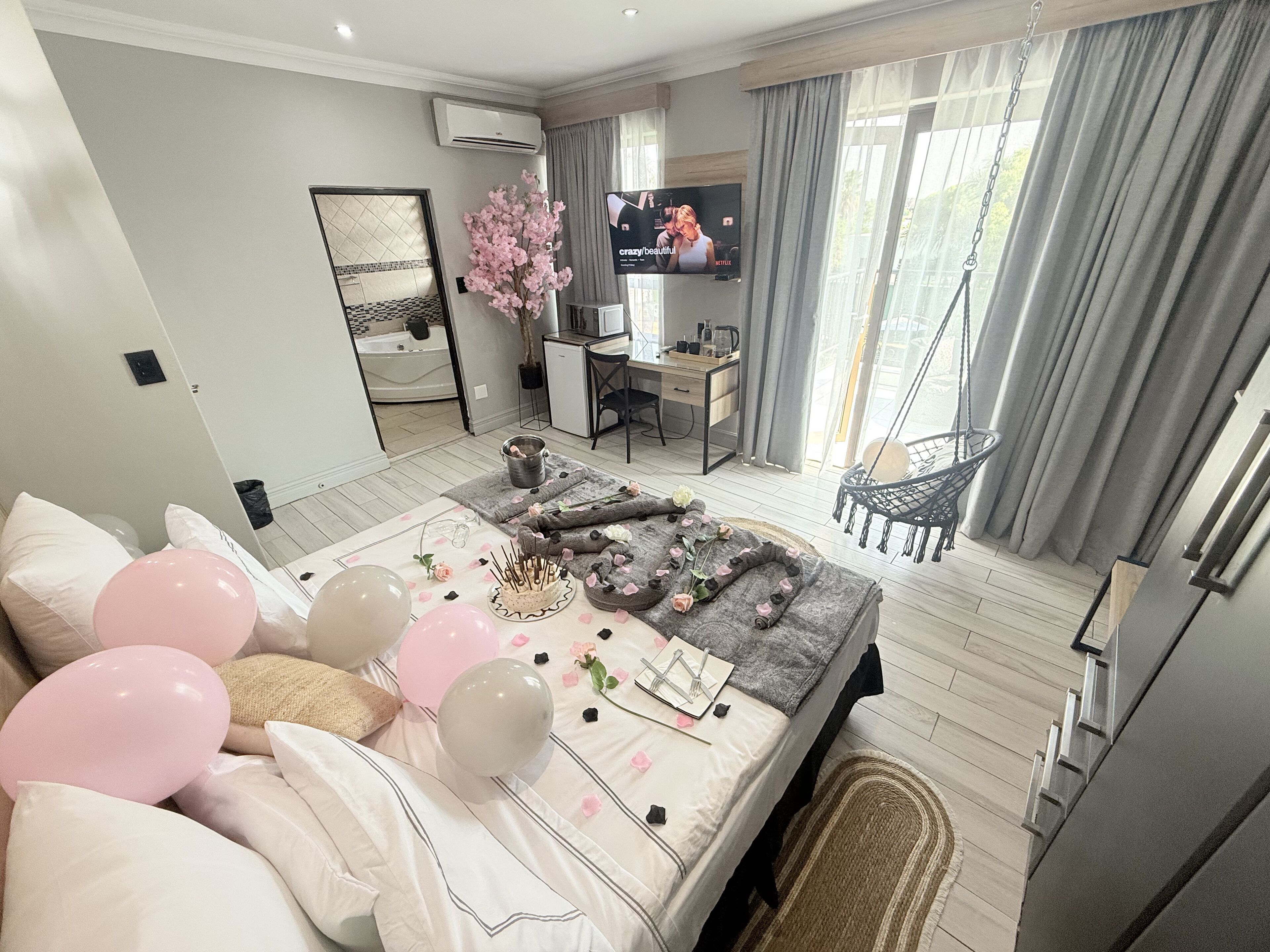 A modern bedroom with a bed, a desk, a TV, and a balcony.