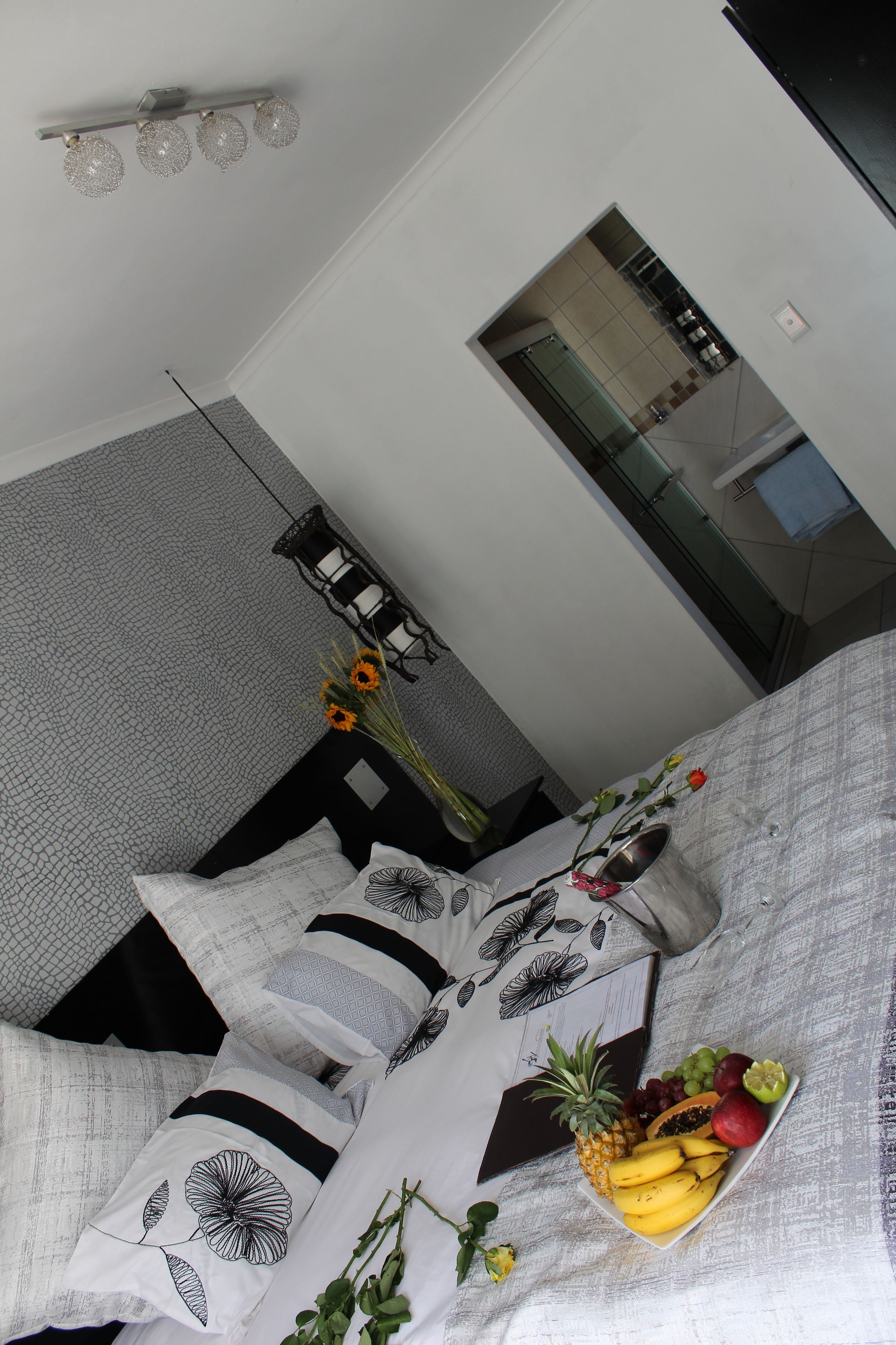 Une chambre d’hôtel moderne, avec un lit, une petite table ornée d’un vase de fleurs et un panier de fruits posé sur la table de chevet.