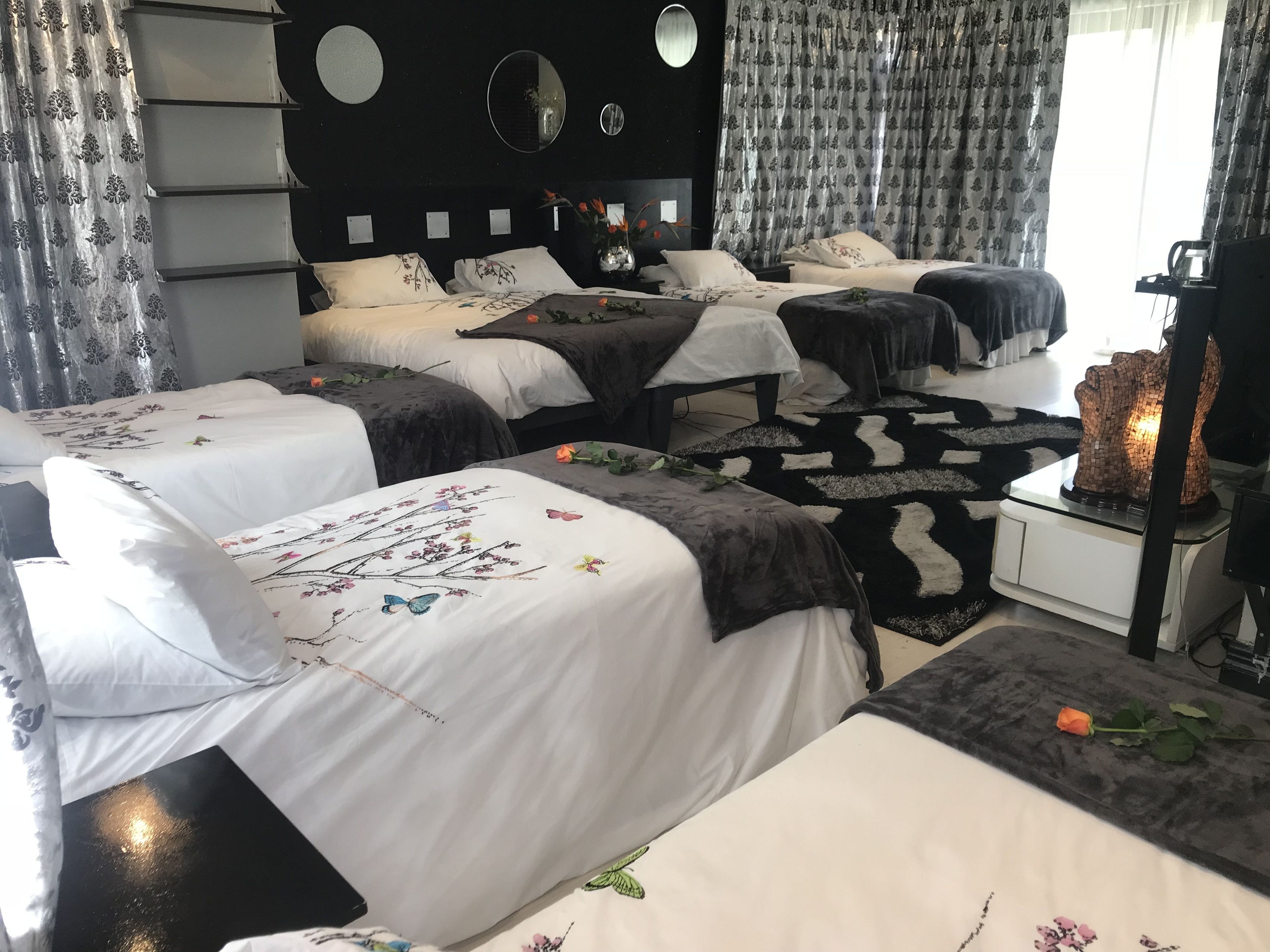 A hotel room with multiple beds, a black headboard, floral bedspreads, a black and white rug, and a decorative wall mirror.