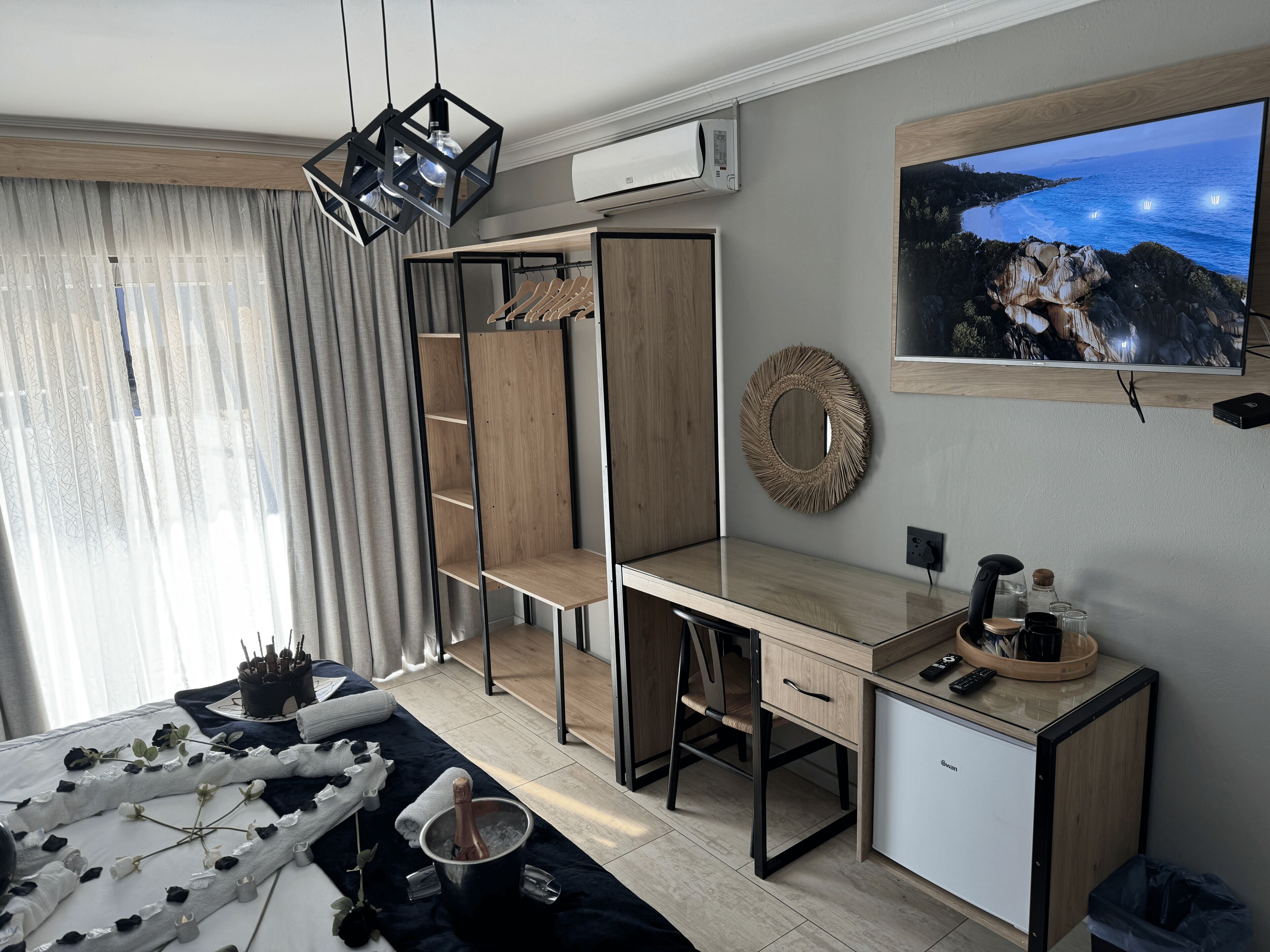 A modern bedroom with a bed, a desk, a wardrobe, a TV, and a view of the sea.