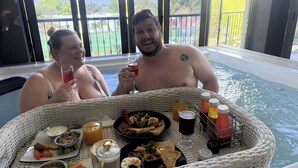 Two people relaxing by a poolside table with a variety of food and drinks. - Africa Paradise Airport Boutique Hotel (Benoni)