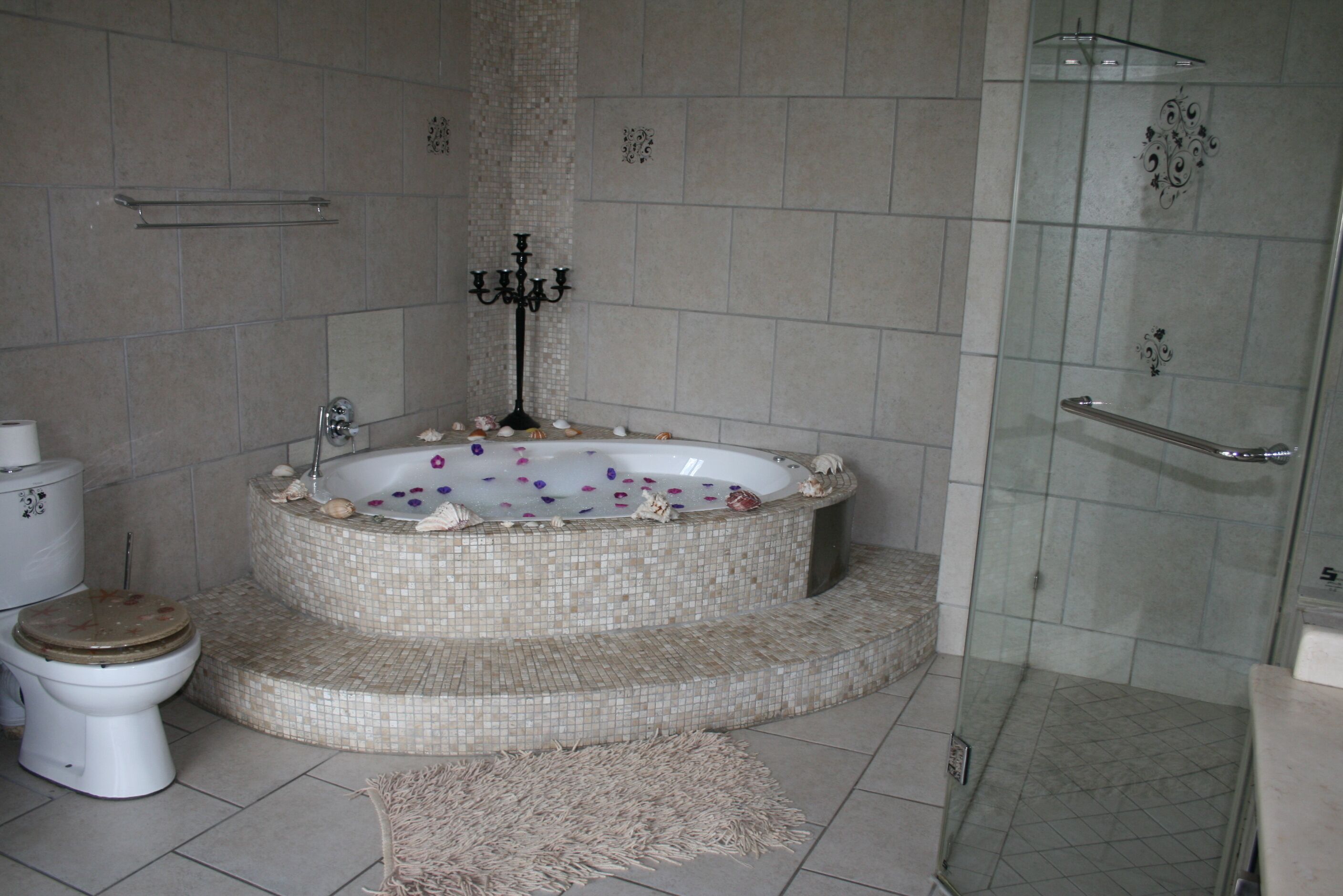Ein Badezimmer mit einer Mosaikbadewanne, einer Duschkabine aus Glas und einem WC.