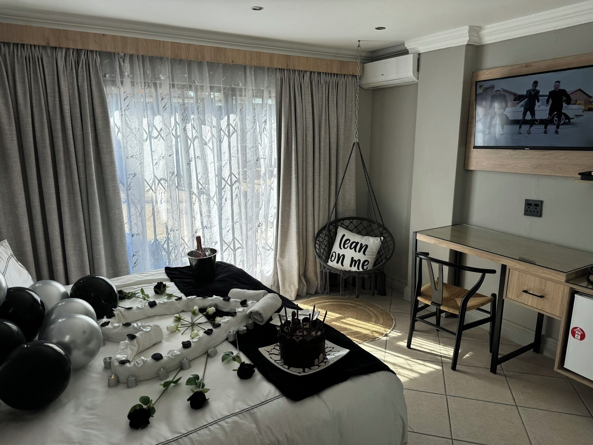 Un dormitorio con una cama, un escritorio, una silla colgante y un televisor en la pared.