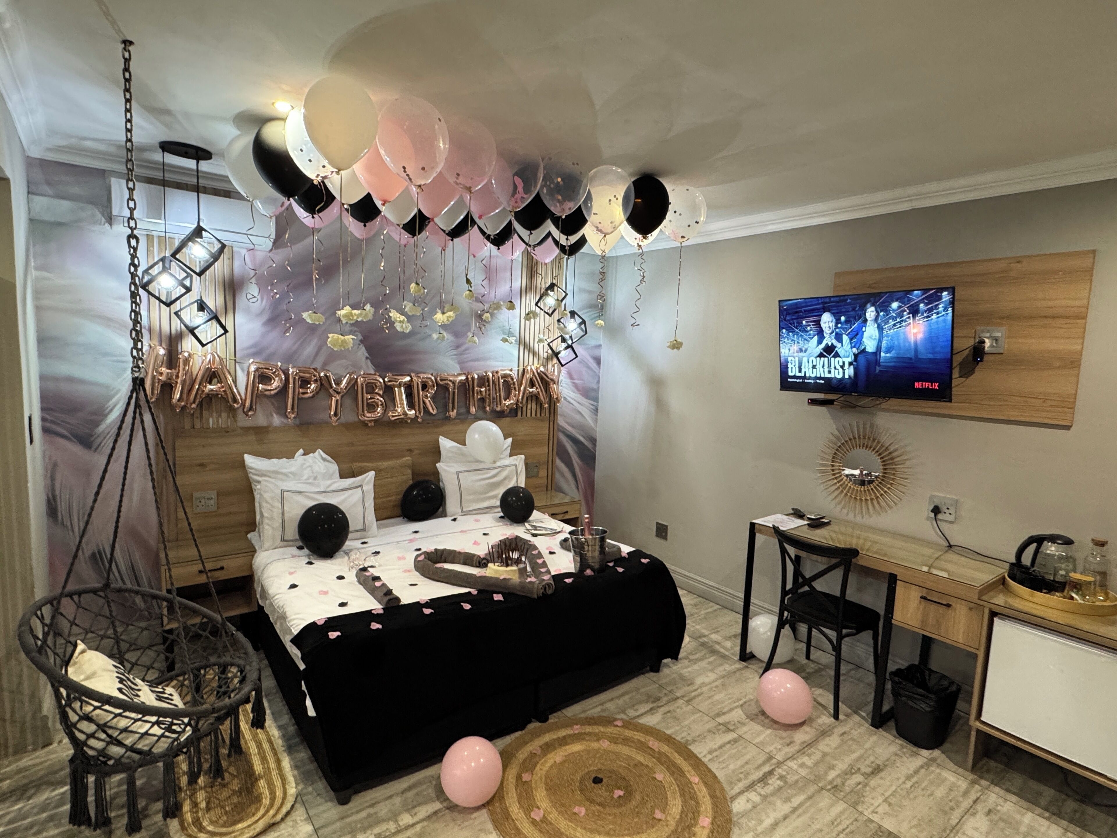 A bedroom with a bed, a desk, a chair, a TV, and balloons.