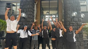 A group of people in front of a building with a stone facade and a sign that reads "OUTIQUE HO". - Africa Paradise Airport Boutique Hotel (Benoni)