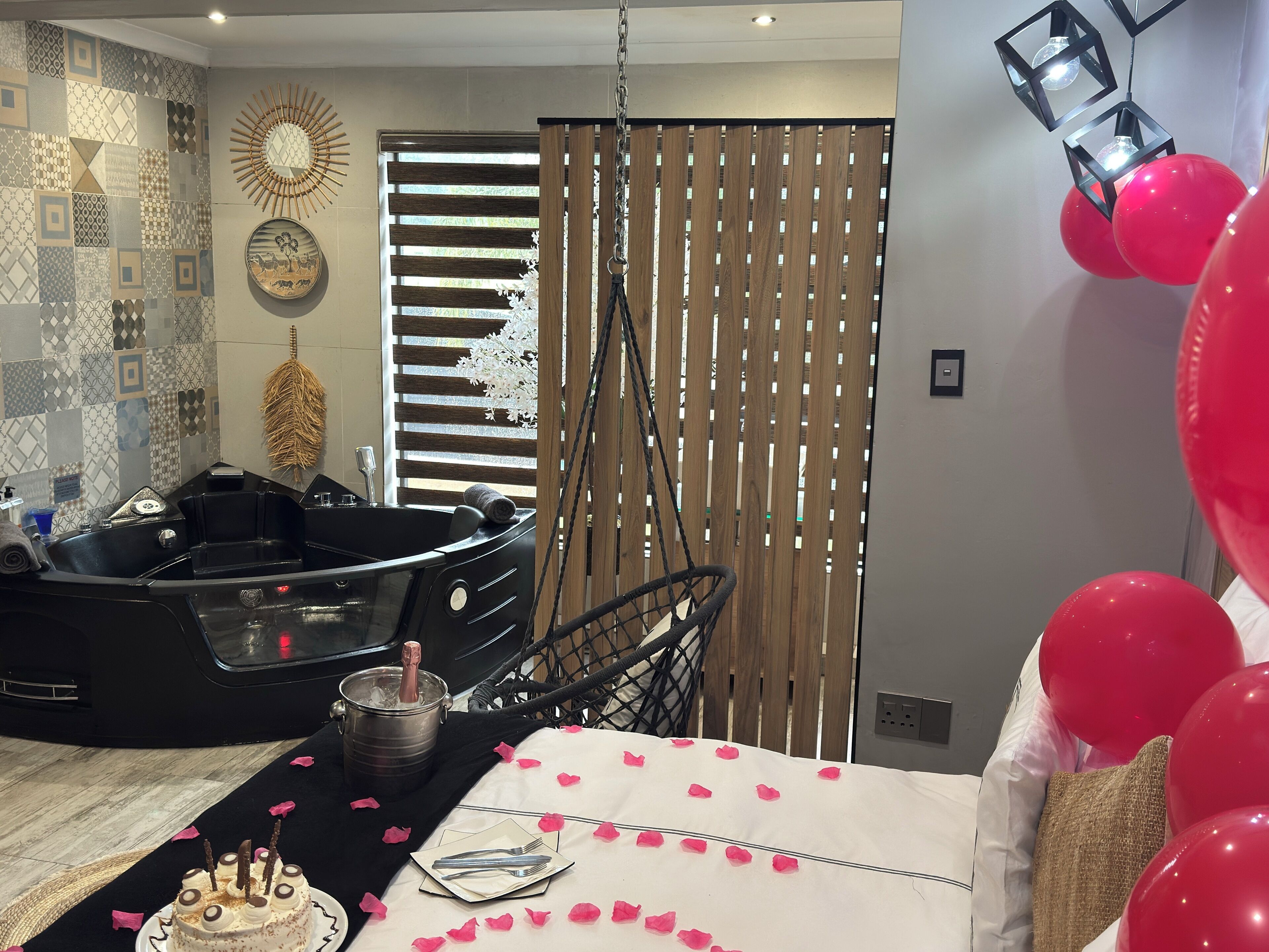 A room with a black bathtub, a dining table with rose petals, and red balloons.