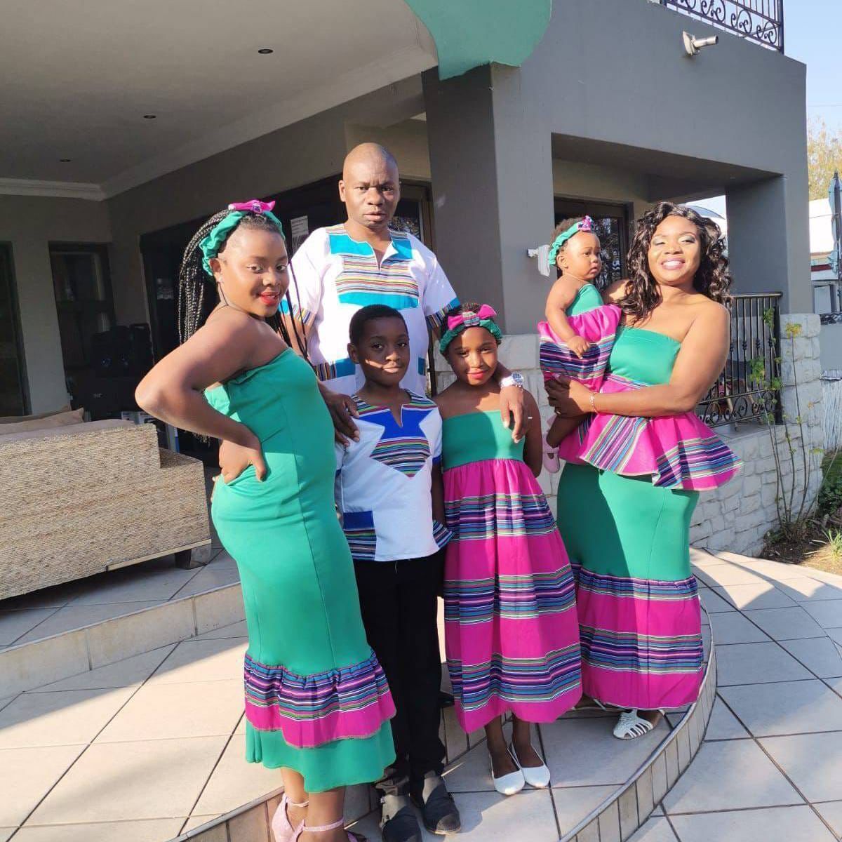 A family of six in front of a modern house with a stone facade and a metal railing.