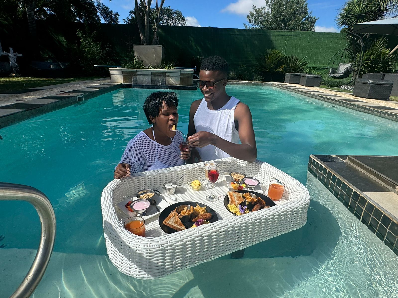 Montaje para comer junto a la piscina con una mesa de mimbre, comida y bebidas.