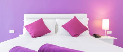 A bed with white bedding and two bright pink pillows, a bedside lamp, and a phone on a white nightstand.