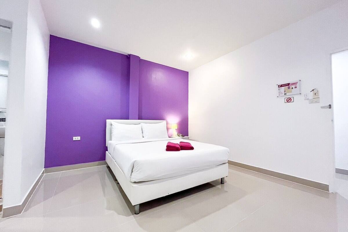 A modern bedroom with a white bed, purple walls, and a white door.