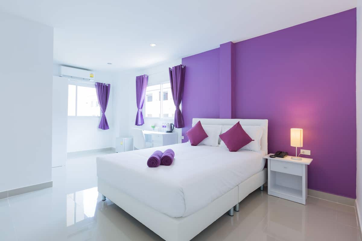 A modern hotel room with a large bed, white walls, and purple accents.