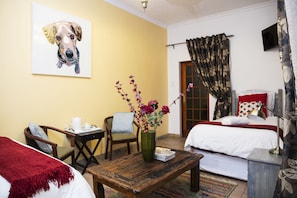 Habitación de hotel con cama, escritorio, silla, mesa de centro, un jarrón con flores y un cuadro de un perro en la pared.