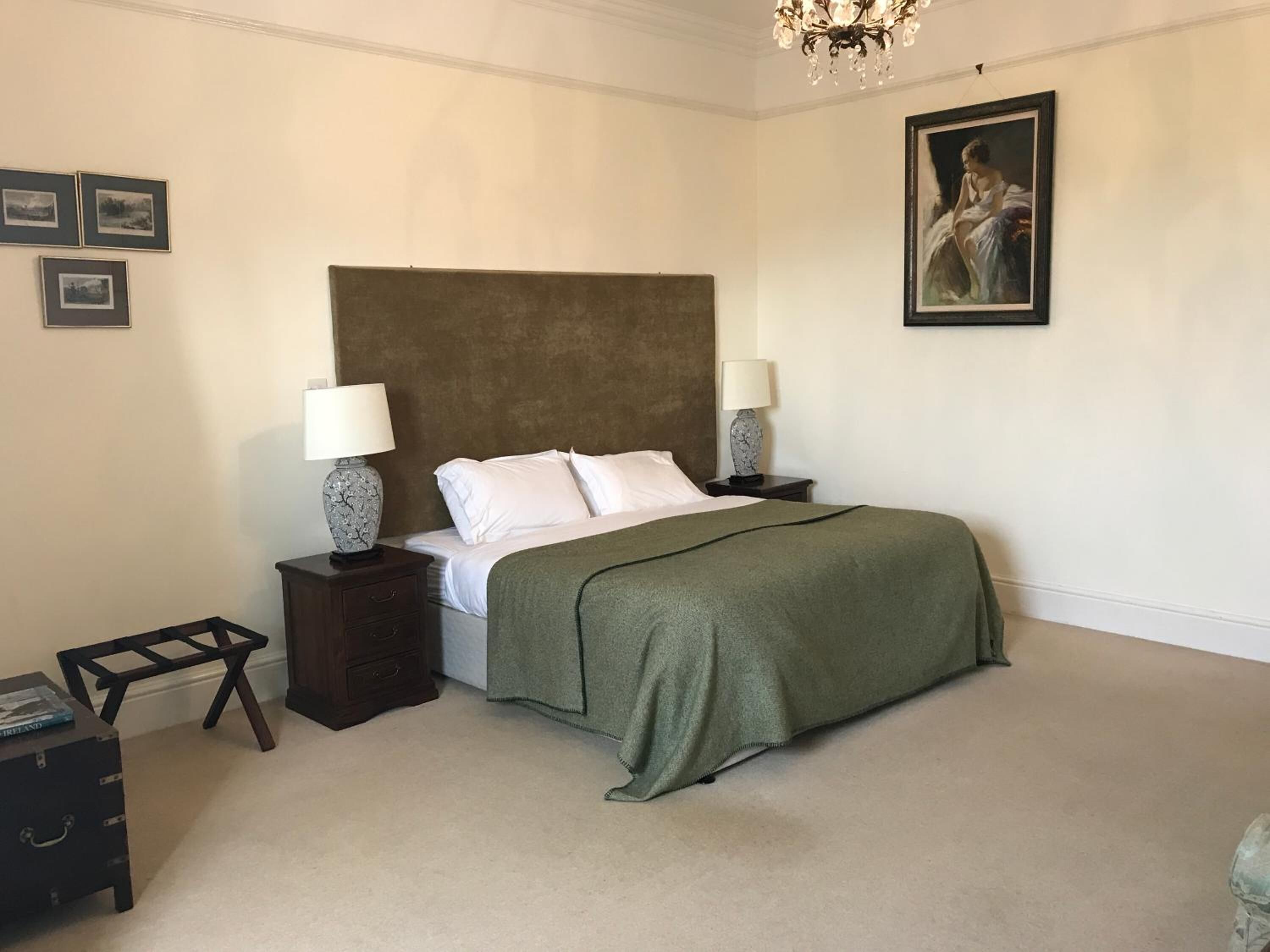 A bedroom with a large bed, two bedside tables with lamps, a small nightstand, a wooden bench, and a chandelier.