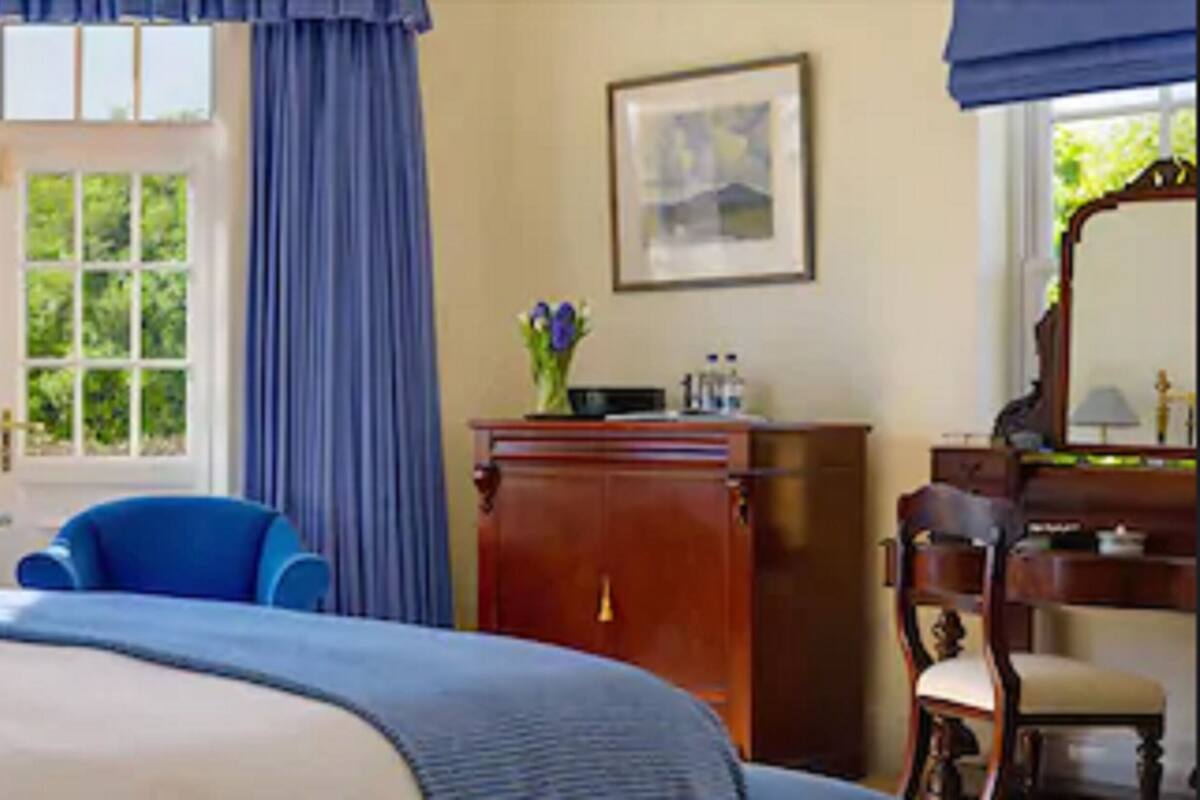 A hotel room with a large bed, a desk, a chair, a wardrobe, and a window with curtains.