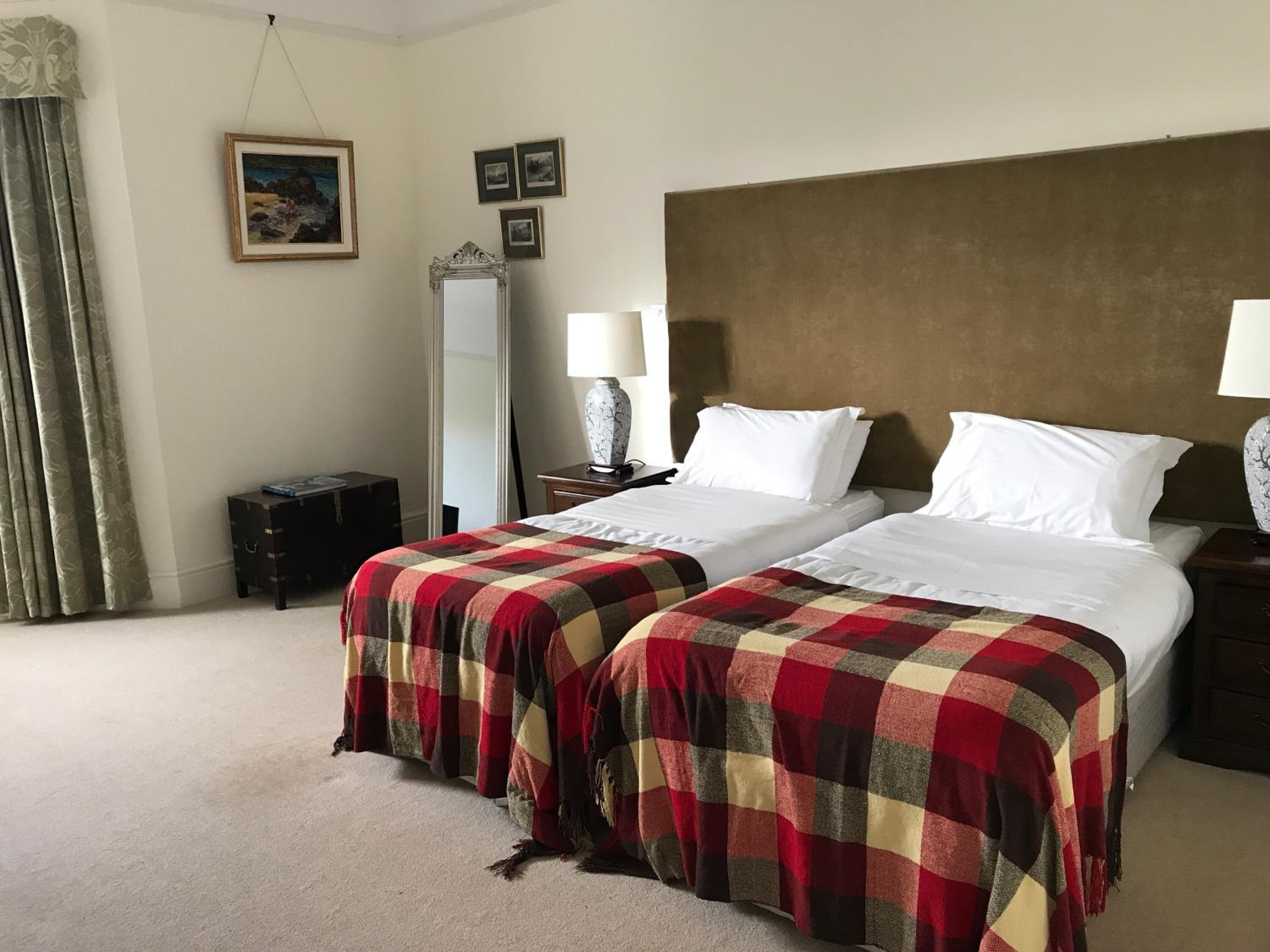 A hotel room with two beds, a large mirror, a nightstand, a lamp, and a dresser.
