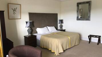 A hotel room with a large bed, two bedside tables with lamps, a chair, a chandelier, a mirror, and a framed picture on the wall.