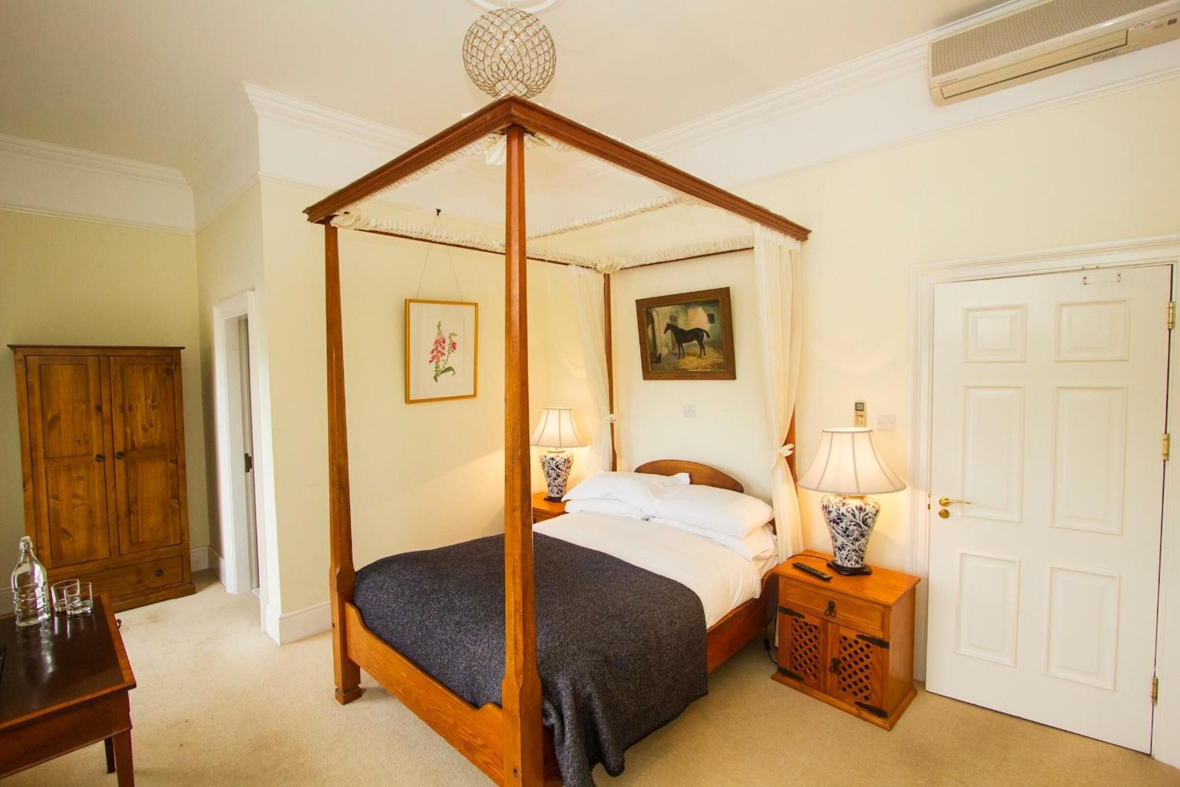 Una cama con dosel de madera, una mesita de noche con una lámpara y una puerta con cerradura.