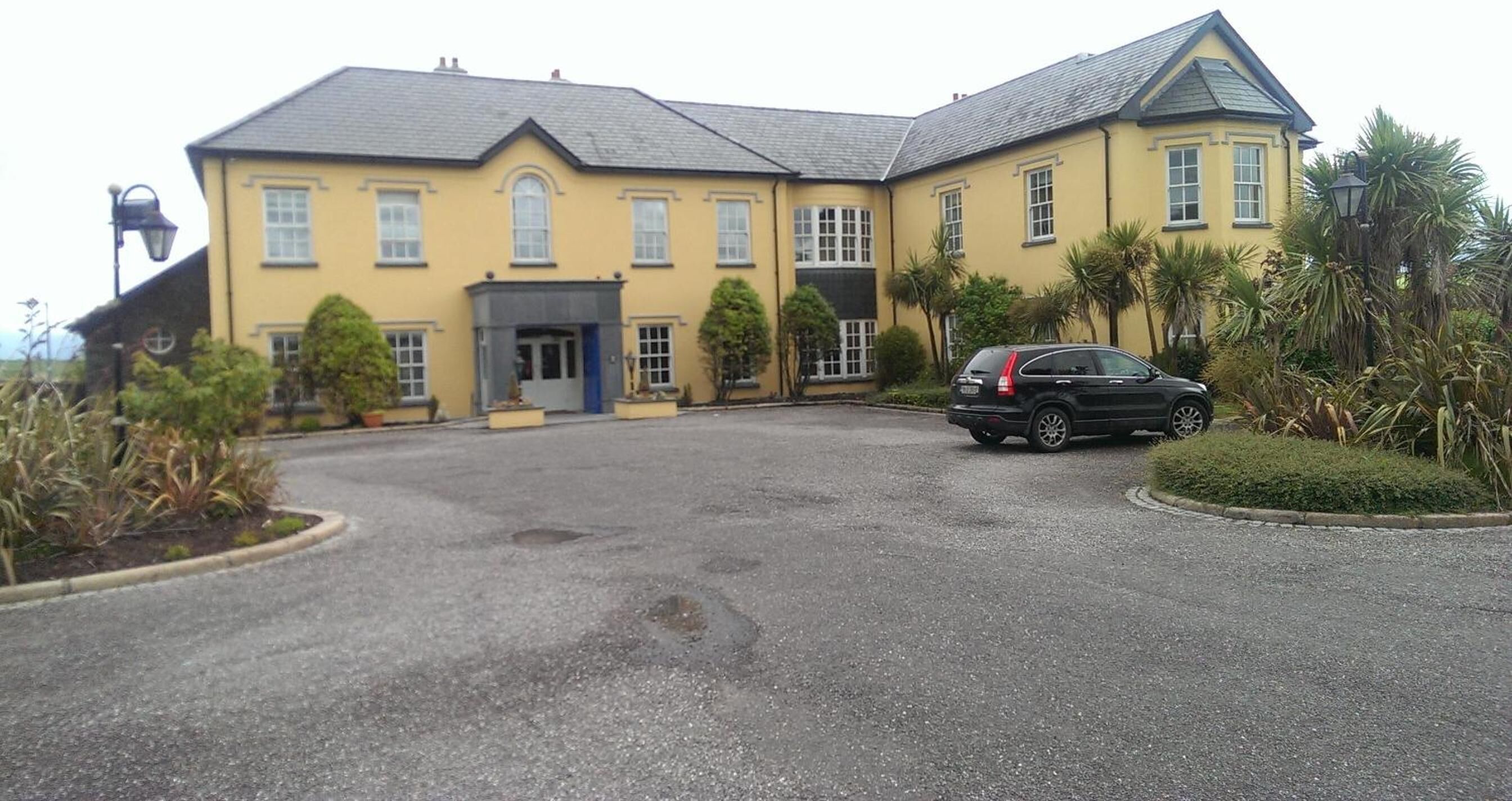 A large yellow building with a grey roof, a driveway, and a parked car.
